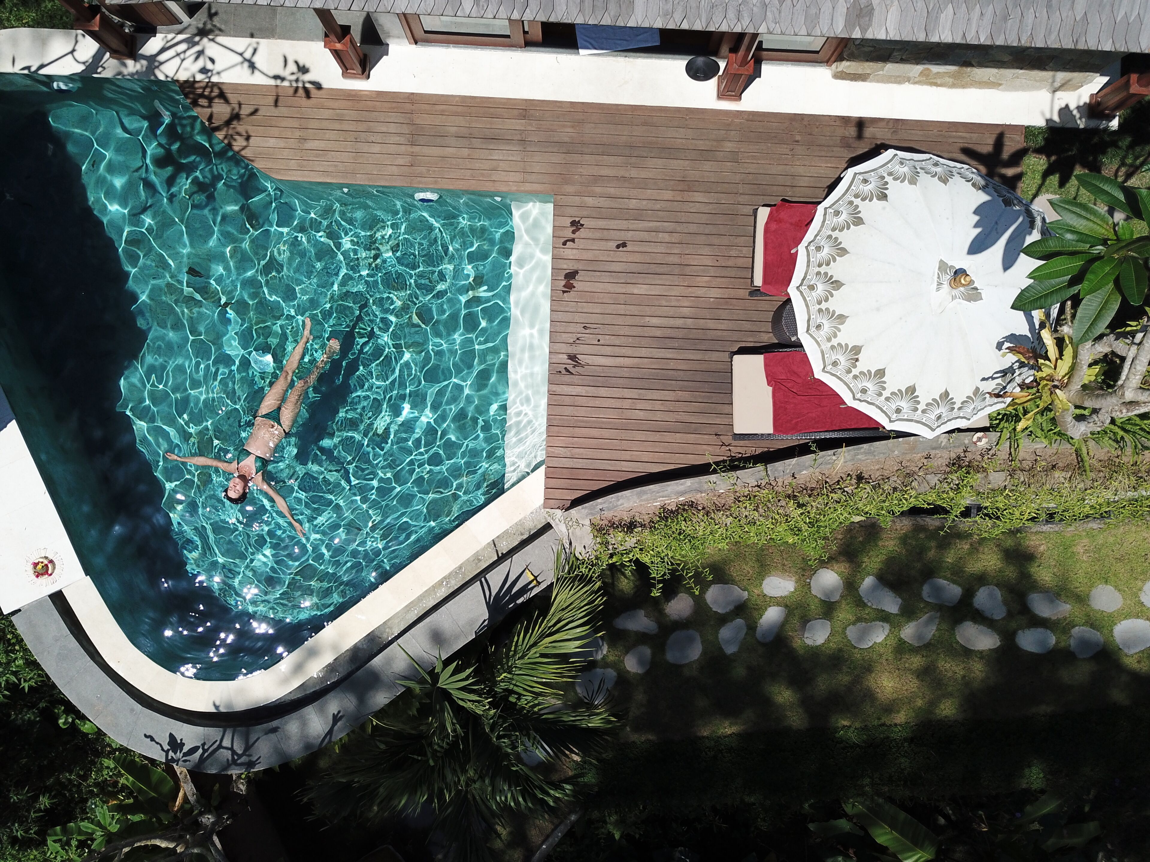 En swimmingpool med en person, omgivet af en træterrasse og et overdækket siddeområde.