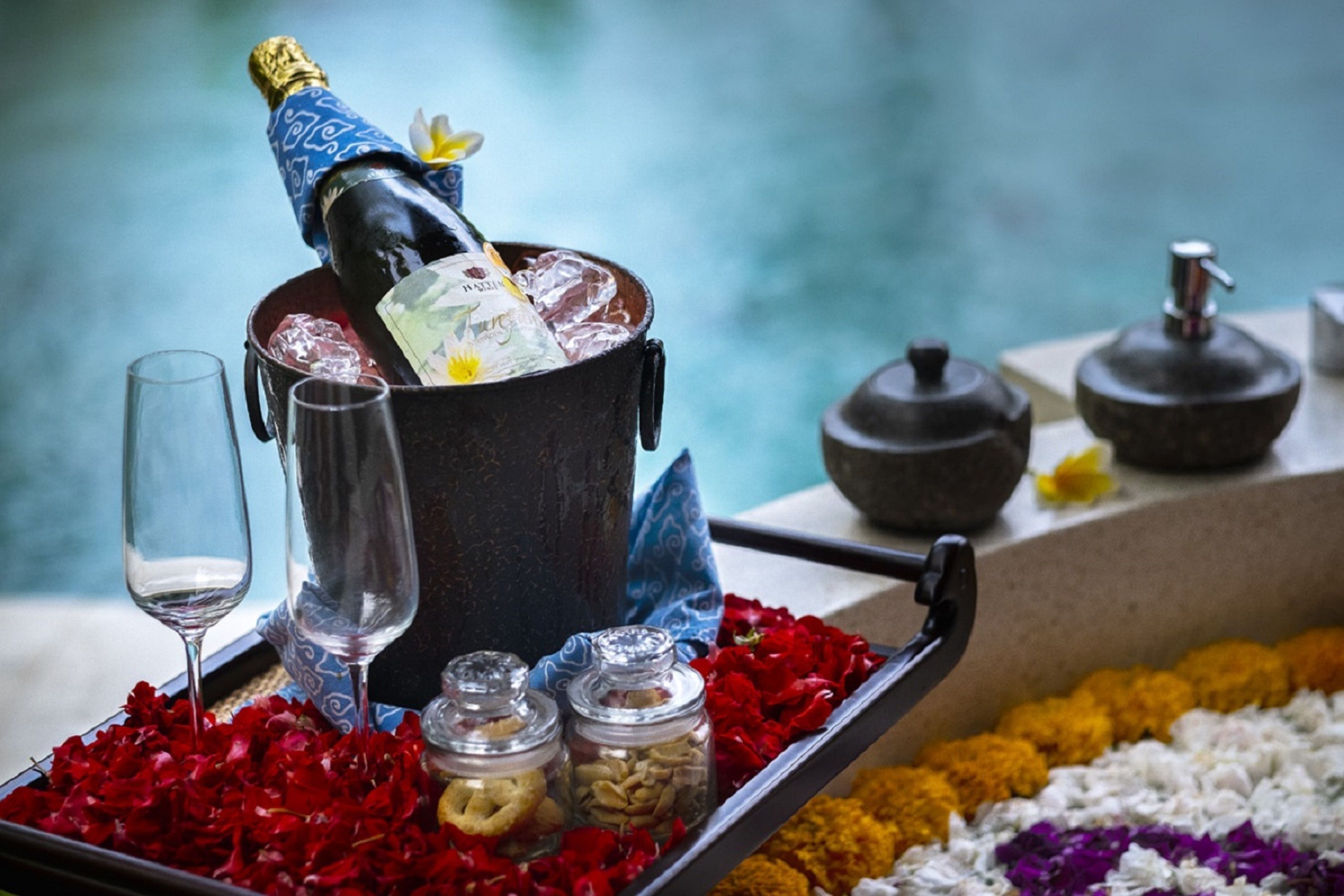 Decoración con una botella de champán, dos copas y una bandeja con pétalos de flores y frascos.