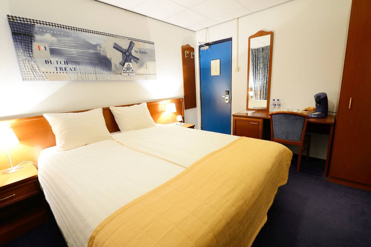 Ein Hotelzimmer mit Bett, Schreibtisch, Stuhl, Spiegel und Tür.