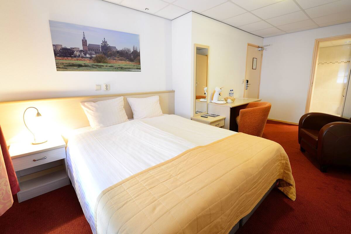 Ein Hotelzimmer mit Bett, Nachttisch, Stuhl, Schreibtisch und einem Bild an der Wand.