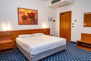 A hotel room with a large bed, bedside lamps, a wooden headboard, a wooden wardrobe, and a floral-patterned carpet. - Prealpi Hotel (San Vendemiano)