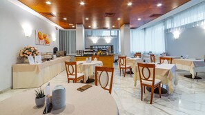 A hotel dining area with tables, chairs, a buffet, and a view of the kitchen. - Prealpi Hotel (San Vendemiano)
