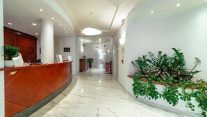 A modern hotel lobby with a wooden reception desk, a marble floor, and a large potted plant. - Prealpi Hotel (San Vendemiano)