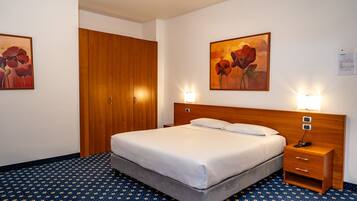 Una habitación de hotel con cama, mesita de noche y dos cuadros en las paredes.