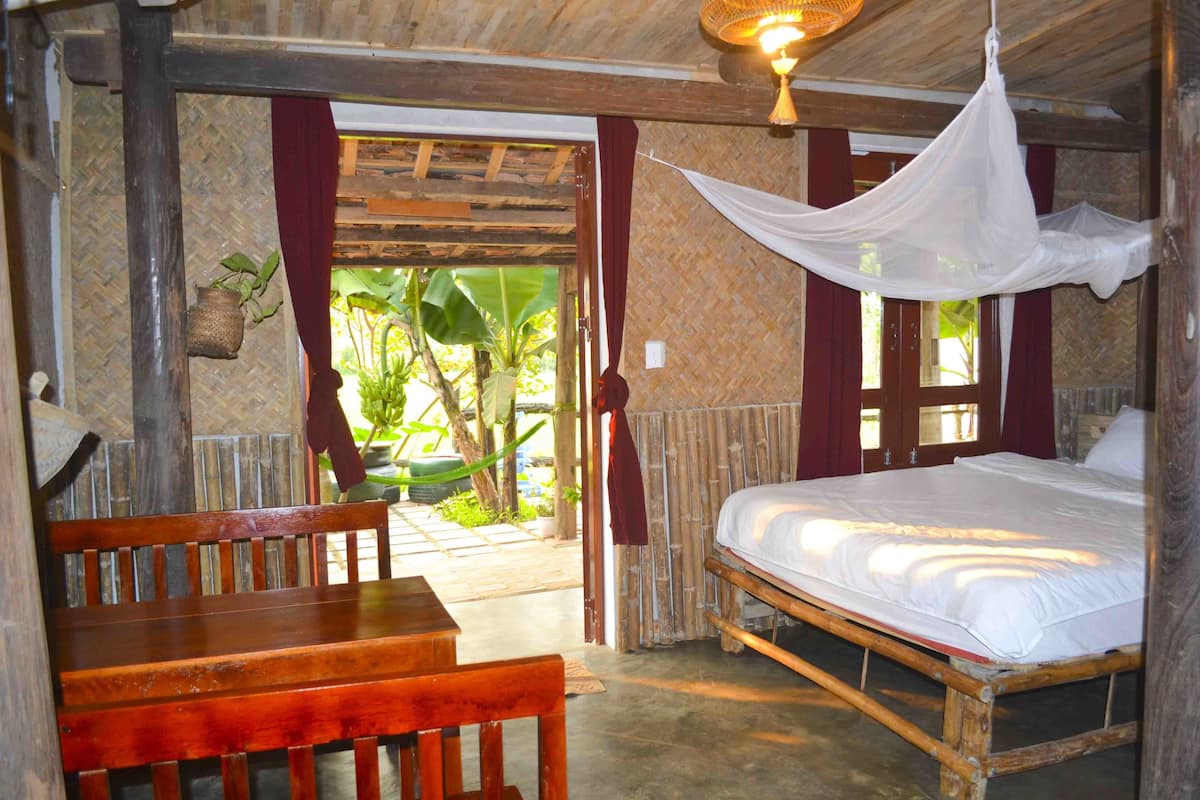 A room with a bed, a wooden bench, and a hanging mosquito net.