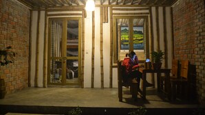 Une pièce chaleureuse avec un plafond en bois, des murs en briques et une grande fenêtre donnant sur un tableau représentant un paysage.