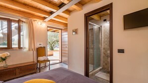 A bedroom with a bed, a chair, a bedside table with a vase, a shower area, and a TV mounted on the wall. - Awesome home in Capodimonte (VT) (Capodimonte (VT))