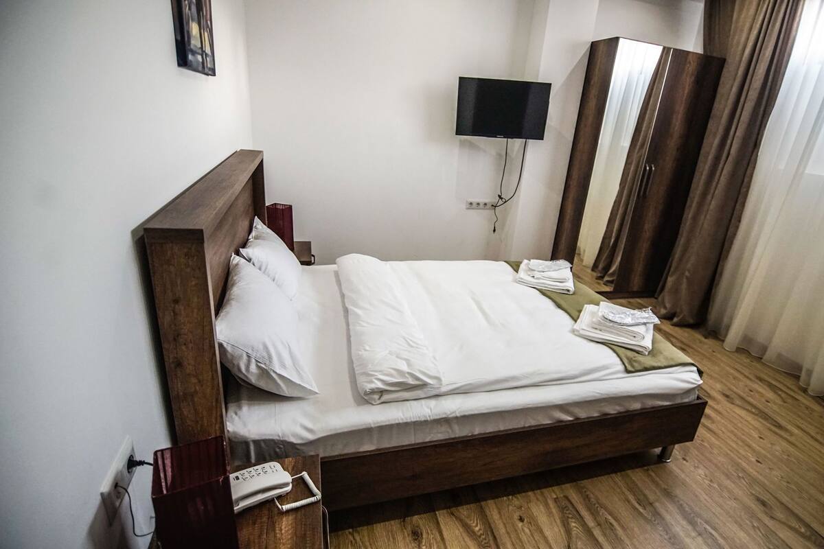 A hotel room with a wooden bed, white bedding, a TV, a wardrobe, and a telephone.
