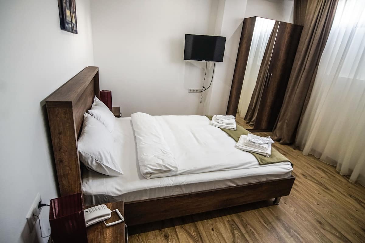 A neatly made bed with white linens, a wooden headboard, a bedside phone, and a TV mounted on the wall.