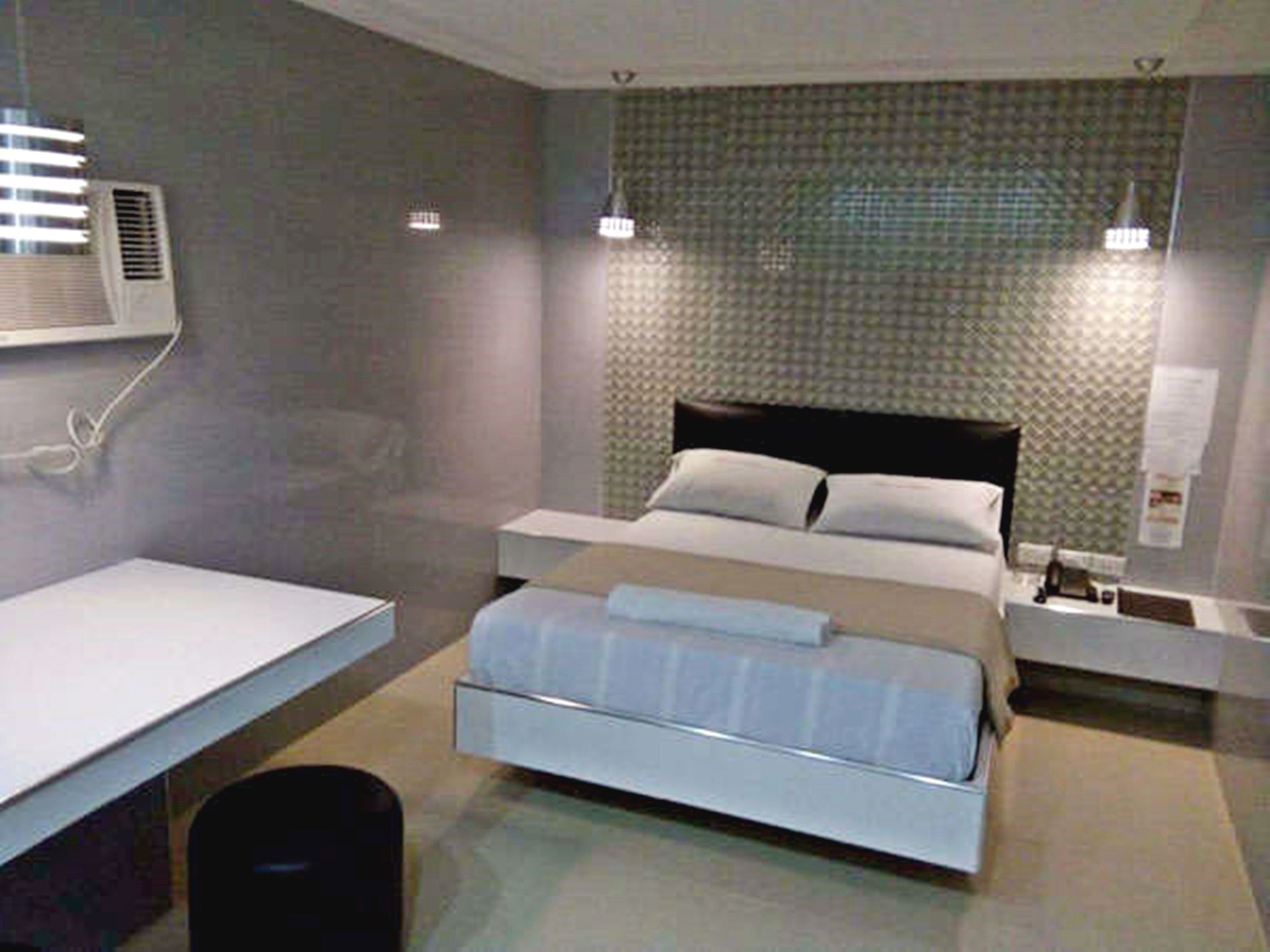 A modern hotel room with a bed, bedside tables, and a desk.