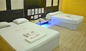 A hotel room with two beds, a small desk, and a wall-mounted control panel.