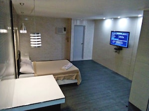 A hotel room with a bed, a desk, a wall-mounted TV, and a door.
