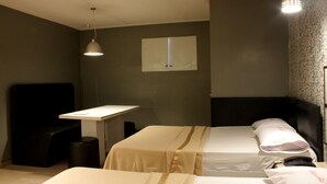 Et hotelværelse med to senge, et skrivebord, en stol og et lille bord.
