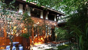 A traditional wooden house with a tiled roof, surrounded by lush greenery and a small garden area. - Demen Renli Hotel (Chengdu)
