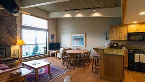 A spacious living area with a wooden floor, a round dining table, and a kitchen with wooden cabinets and a black microwave.