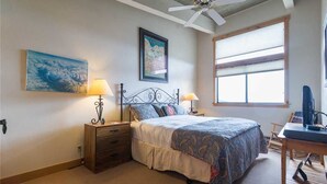 A bedroom with a bed, two bedside tables, a desk, a ceiling fan, and a window.