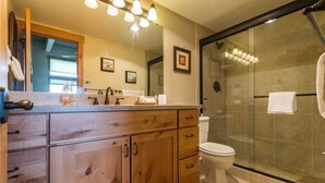 A bathroom with wooden cabinets, a sink, a toilet, and a glass-enclosed shower.