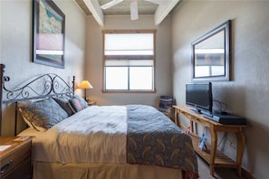 A bedroom with a bed, a TV on a wooden stand, a window, and a painting on the wall.