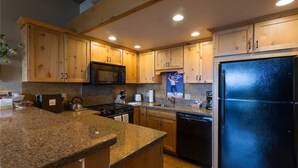 A kitchen with wooden cabinets, granite countertops, a black refrigerator, and a microwave.