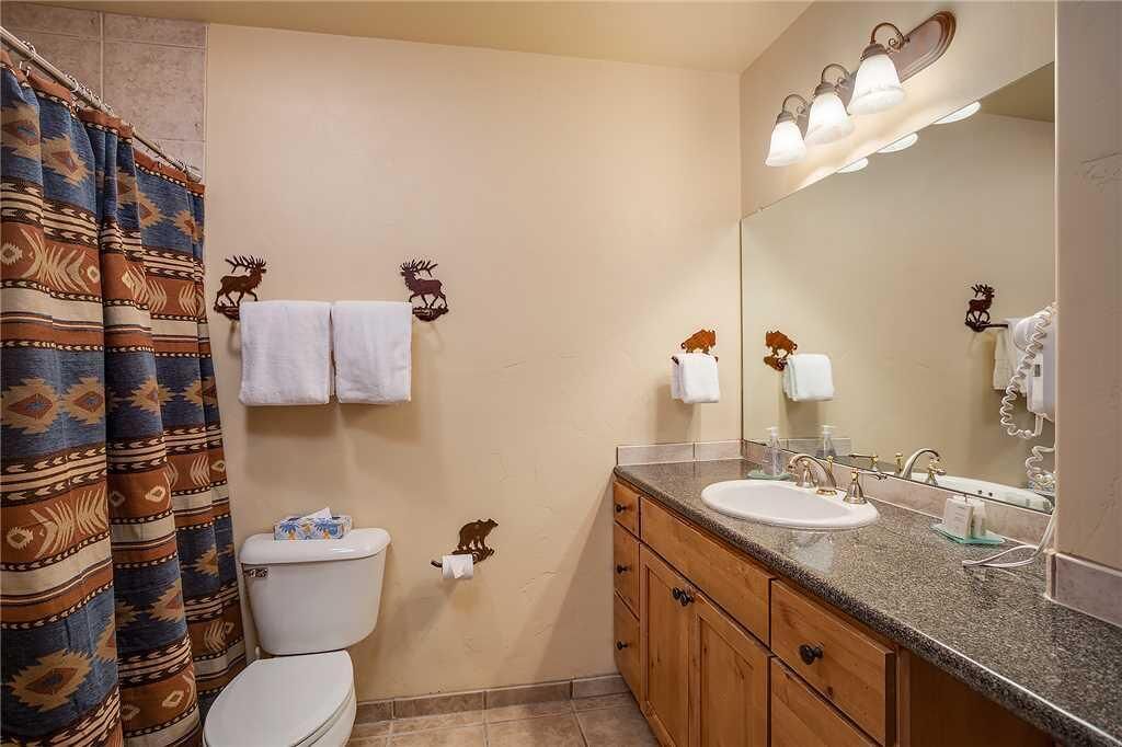 Un bagno con tenda doccia, un water, un lavabo con specchio e porta asciugamani a parete.