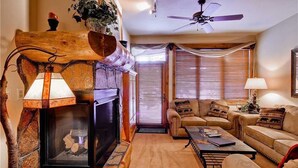 Un salon chaleureux avec une cheminée, un ventilateur de plafond et un canapé agrémenté de coussins à motifs.
