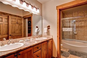 A bathroom with wooden cabinets, a double sink, a large mirror, and a glass-enclosed shower.