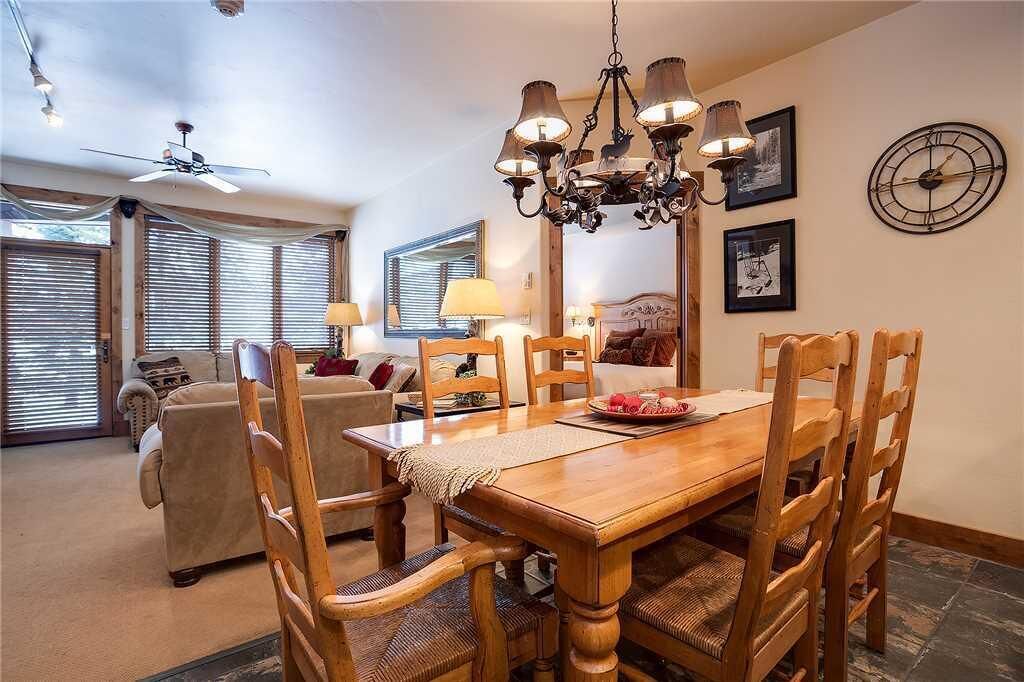 A dining area with a wooden table and chairs, a chandelier, and a clock on the wall.