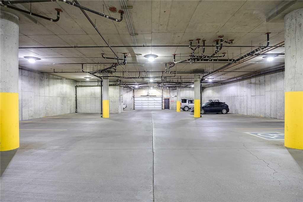 Un aparcamiento con pilares de hormigón, un coche y tuberías visibles en el techo.