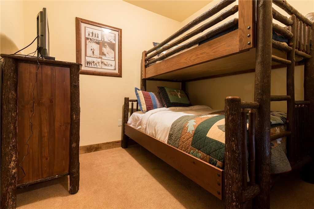 A bunk bed with a wooden frame, a small wooden desk, and a framed picture on the wall.