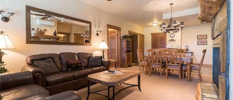 A cozy living room with a leather sofa, a coffee table, and a dining area with wooden chairs and a chandelier.