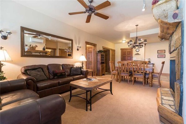A cozy living room with a leather sofa, a coffee table, and a dining area with wooden chairs and a chandelier.