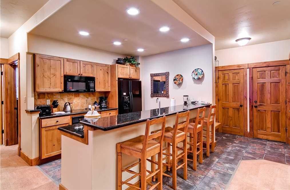 A kitchen with wooden cabinets, a black countertop, and a bar area with stools.