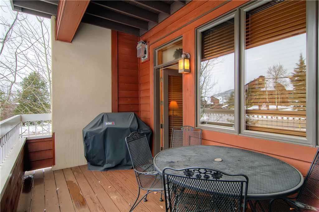 Un patio exterior techado con una mesa, sillas, una parrilla de barbacoa y vistas a un paisaje nevado a través de amplios ventanales.
