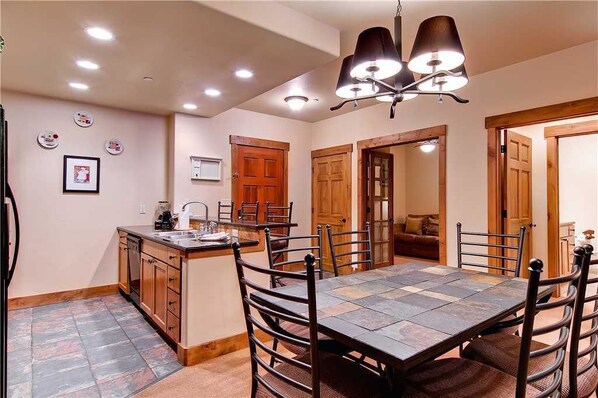 A dining area with a large table, chairs, and a kitchen area with a sink and cabinets.
