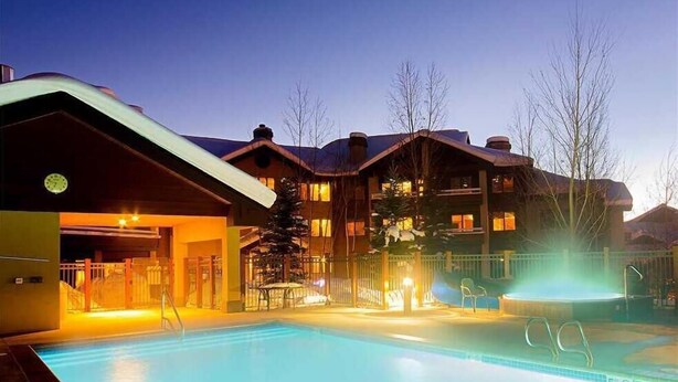 A hotel with a swimming pool, a covered entrance, and a ski lift visible in the background.