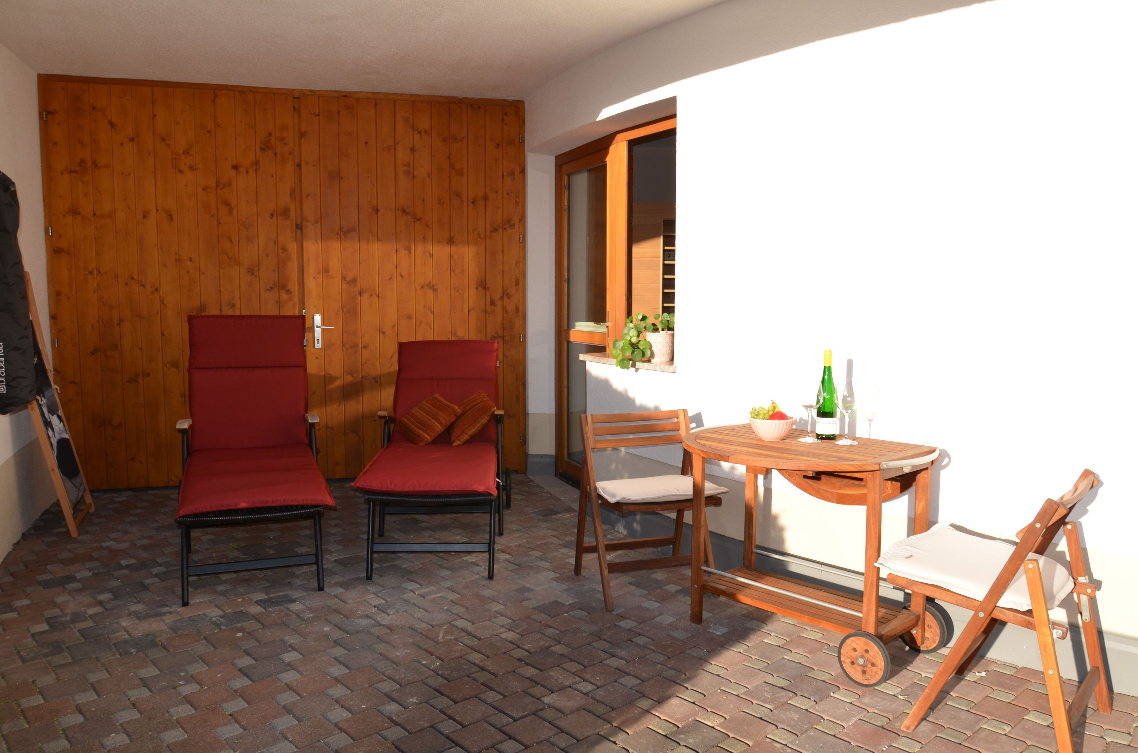 Una habitación con pared de madera, una silla roja, una mesa de madera con sillas y una ventana con vistas.