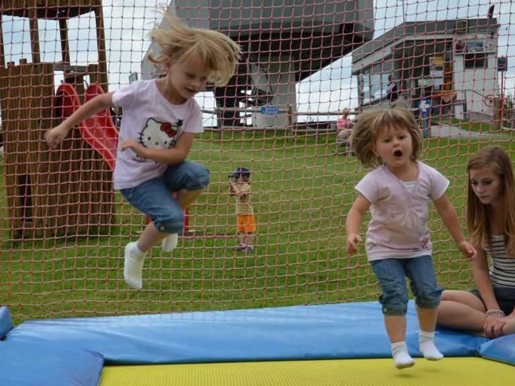 Un trampoline doté d’un filet de protection, un enfant qui saute et un autre enfant qui regarde.