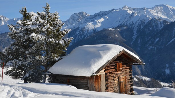 A wooden cabin with a snow-covered roof, surrounded by snow-covered mountains and trees. - Apart Franzi Top 1 - Apart Franziska (Kauns)