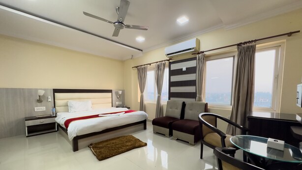 Una habitación de hotel con cama, escritorio, silla, sofá, ventilador de techo y ventana con cortinas.