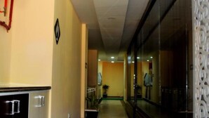 Un pasillo de hotel con suelo de mármol, un mostrador de recepción con un abanico rojo y un panel decorativo en la pared.