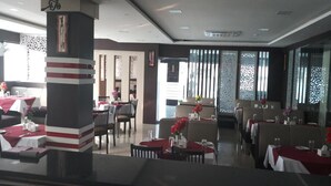 Un restaurante con varias mesas y sillas, un pilar decorativo y cortinas con diseños.