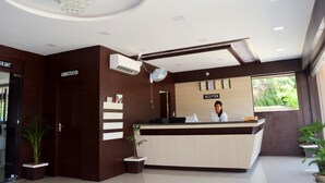 Zona de recepción de un hotel con recepcionista, mostrador de recepción, un reloj y un ventanal grande.