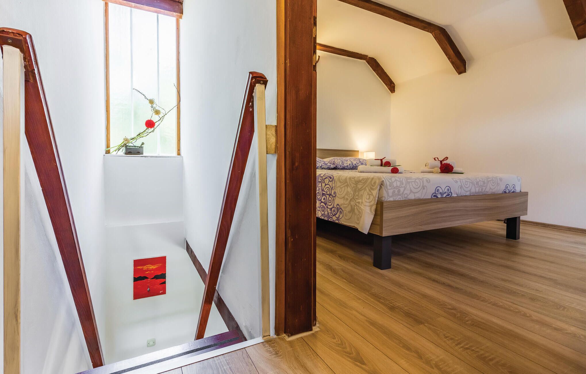 Ein Schlafzimmer mit Holzboden, einem Bett mit gemustertem Überwurf und einem Fenster mit Blick ins Freie.