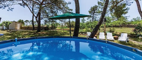 A swimming pool with a green umbrella, surrounded by trees and outdoor furniture.