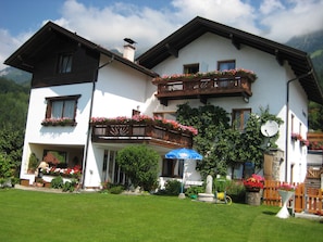 A two-story building with balconies, a garden, and a mountain backdrop.