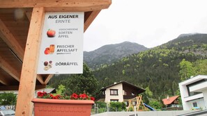 Un cartel publicitario muestra variedades de manzanas locales, una estructura de madera y un paisaje montañoso con edificios.