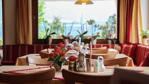 A restaurant with tables set for dining, potted plants, and a view of the sea.
