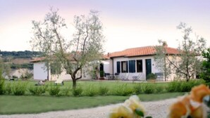 A white building with a red-tiled roof, surrounded by a well-maintained lawn and trees. - Saturnia Glamping - Seme di Carota (Manciano)