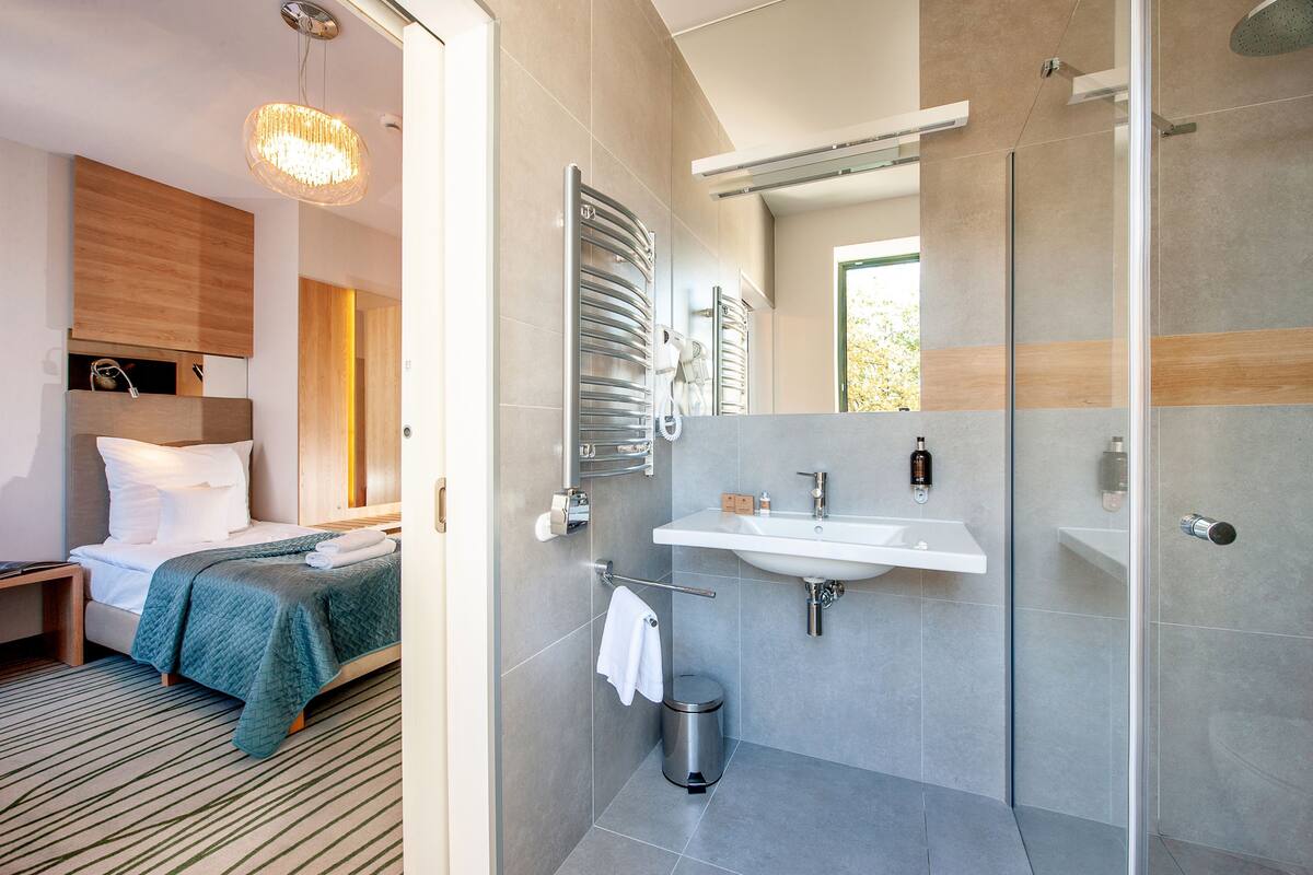 Une chambre d’hôtel moderne équipée d’un lit, d’une table de chevet et d’une salle de bain avec un lavabo, un miroir et une douche.