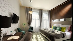 Une chambre d’hôtel avec un lit, un bureau et une chaise, une télévision et une fenêtre avec des rideaux.